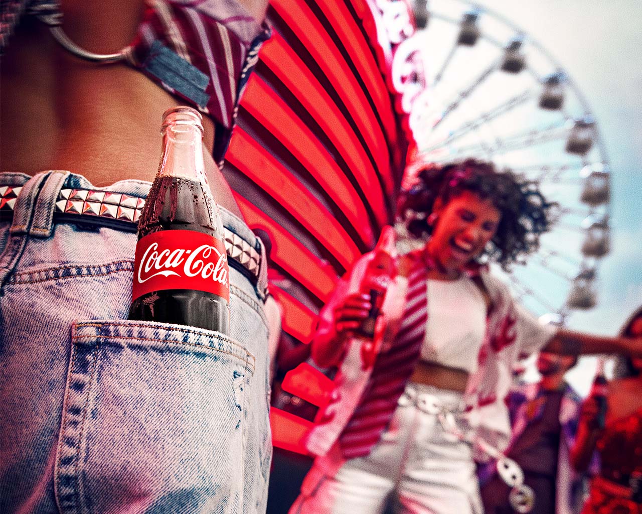 Um close-up de uma garrafa de Coca-Cola saindo do bolso traseiro de um jeans desgastado, com o fundo de uma feira iluminada e pessoas desfrutando do ambiente festivo.