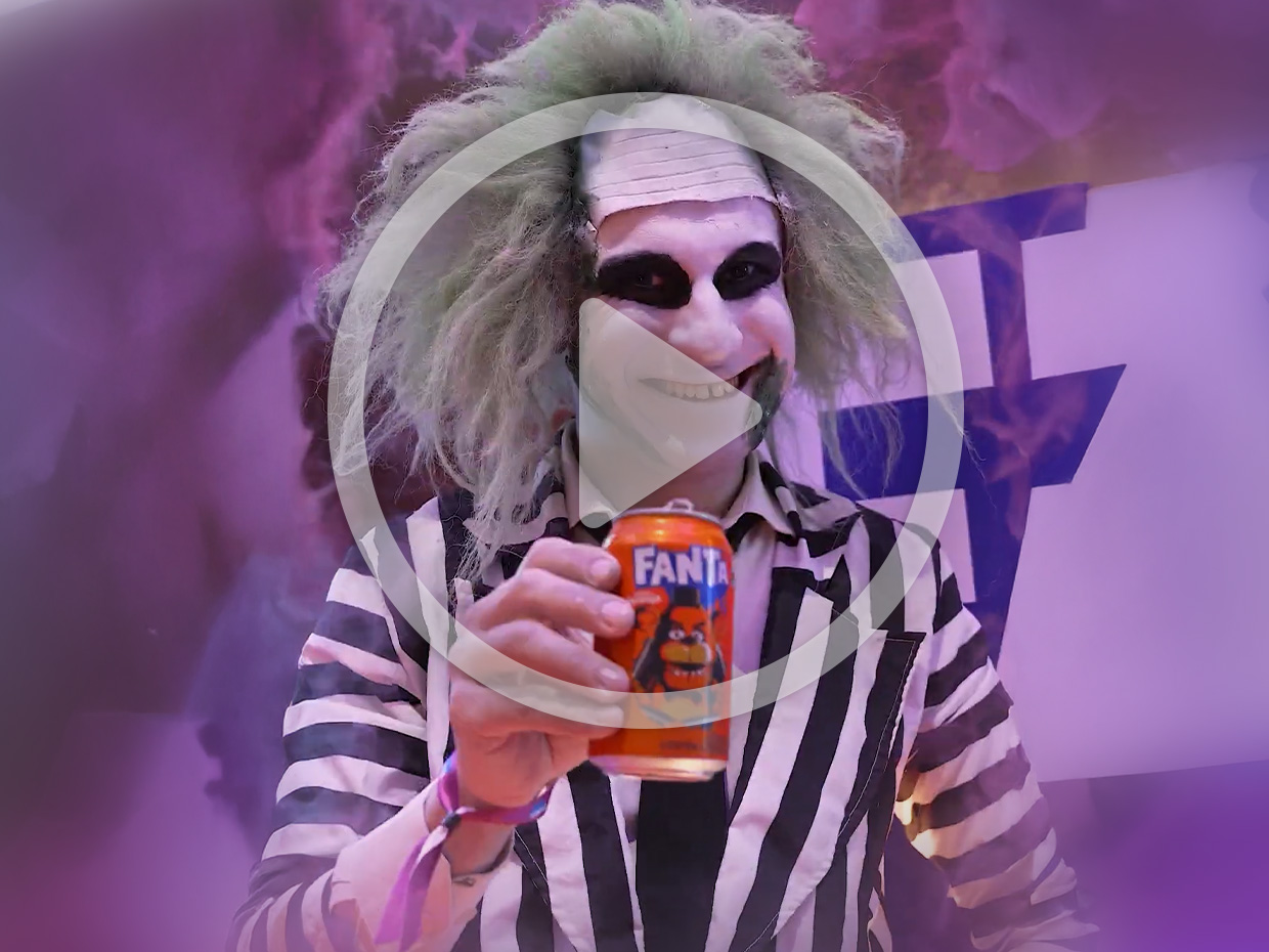 Pessoa fantasiada de Beetlejuice sorrindo, segurando lata de Fanta laranja.