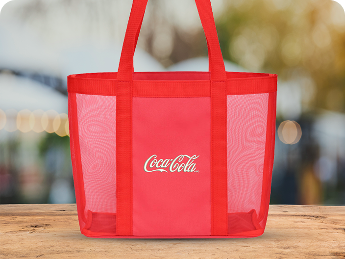 A bright red Coca-Cola mesh tote bag with the script logo, a prize from the Outdoor Activities pool, sits on a wooden surface.