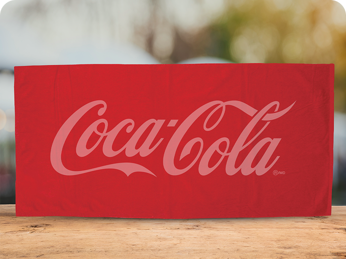 Une serviette de plage rouge Coca-Cola pliée, ornée d'un grand logo ton sur ton, offerte comme prix Activités en plein air.