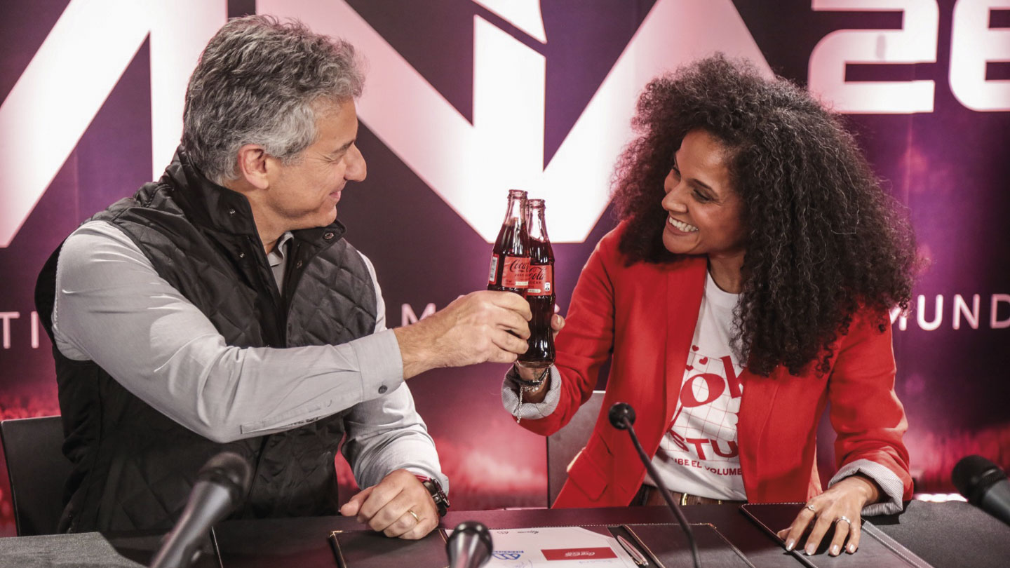 Un hombre y una mujer brindan con botellas de Coca-Cola Zero en un evento.