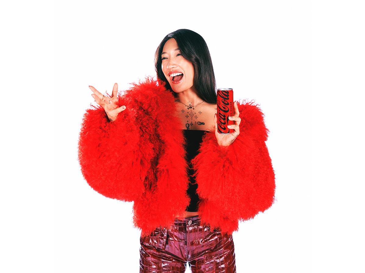 Peggy Gou riendo, vistiendo una chaqueta de piel roja, en un fondo blanco.