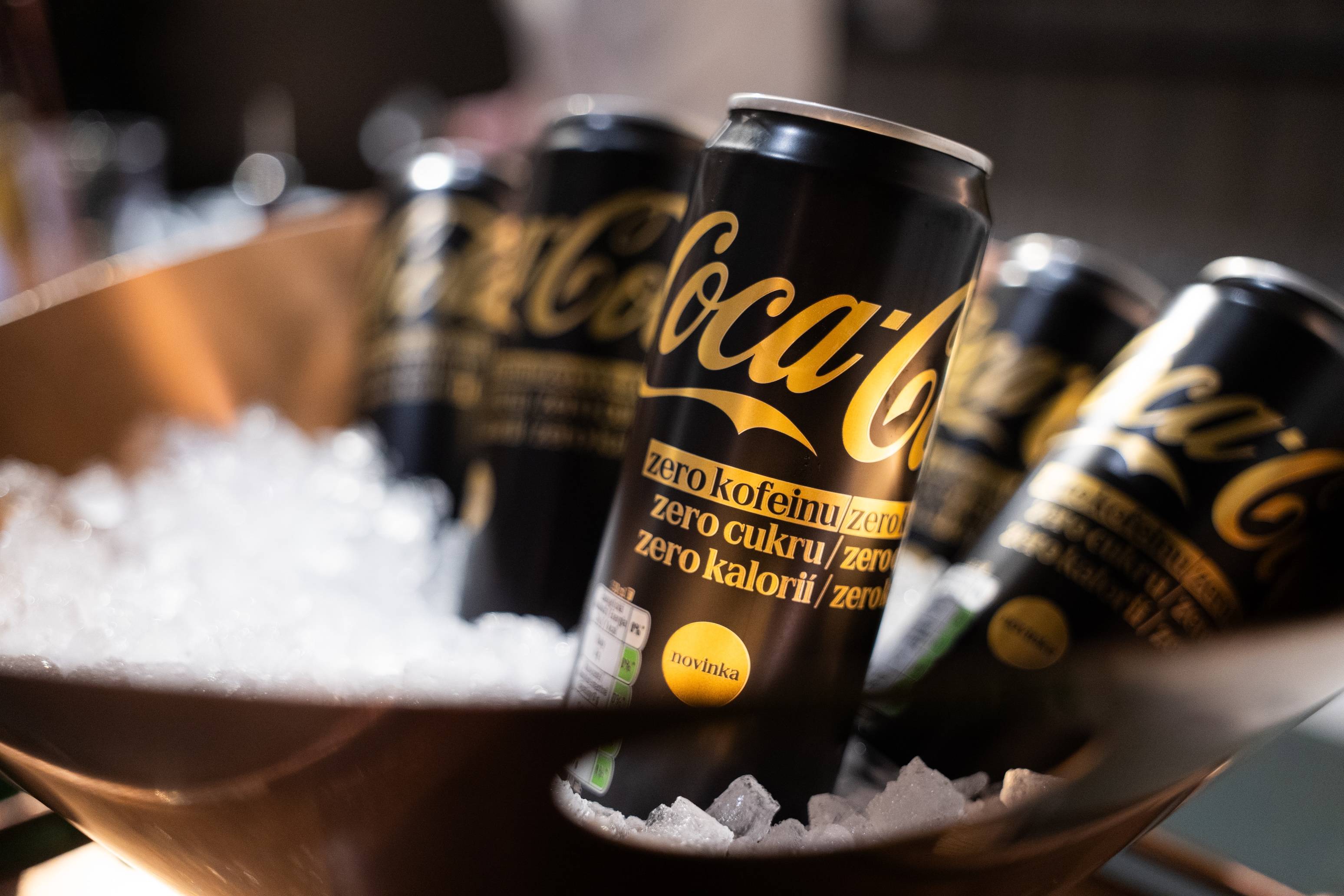„Plechovky Coca‑Cola Zero vychlazené v misce s ledem, osvěžující nealkoholický nápoj bez cukru s černo‑zlatým obalem, připravený k podávání“