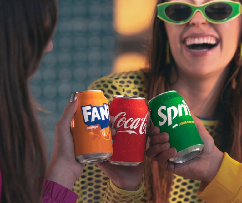 En gruppe venner skåler med dåser af Coca‑Cola, Fanta og Sprite.