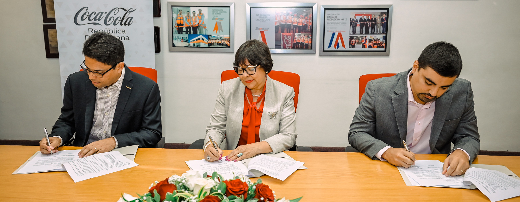 Tres personas firmando documentos sobre una mesa