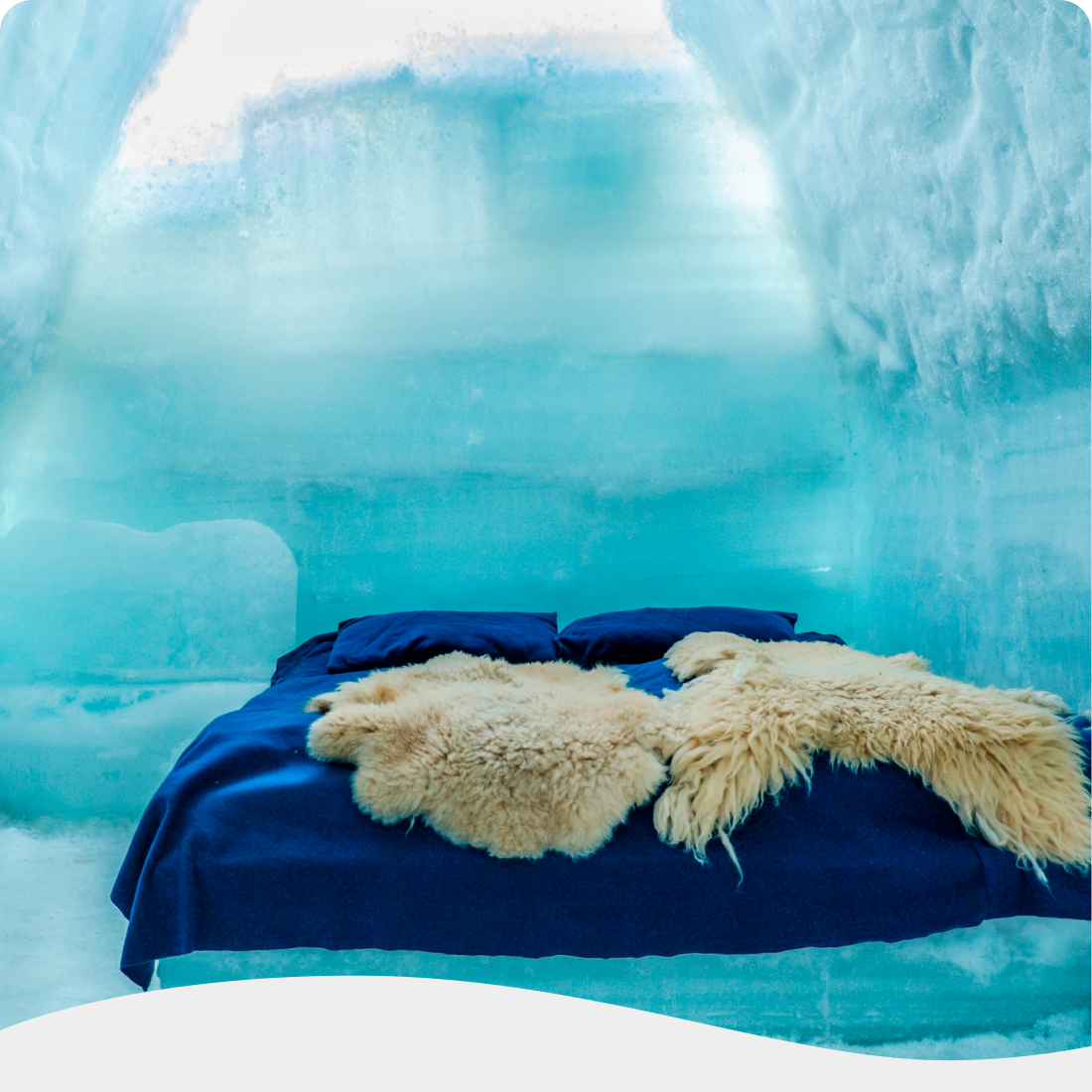 Lit recouvert de couvertures en fourrure, dans une chambre aux murs de glace bleue. |  Bed met bontdekens in een kamer met blauwe ijsmuren.
