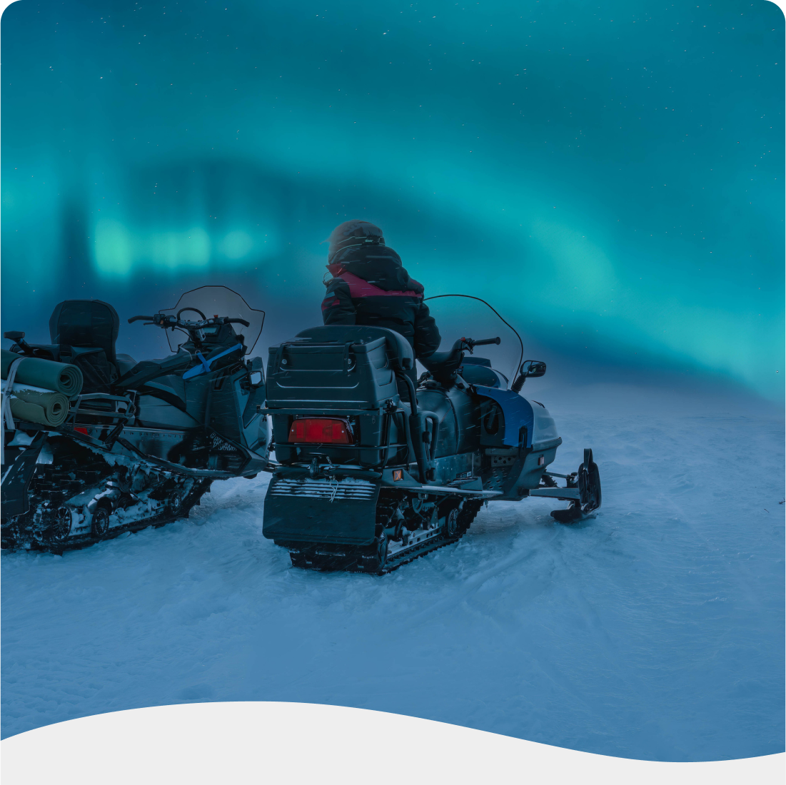 Personne assise sur une motoneige dans un paysage enneigé, avec des aurores boréales illuminant le ciel. | Persoon op een sneeuwscooter in een besneeuwd landschap, met noorderlichten die de lucht verlichten.