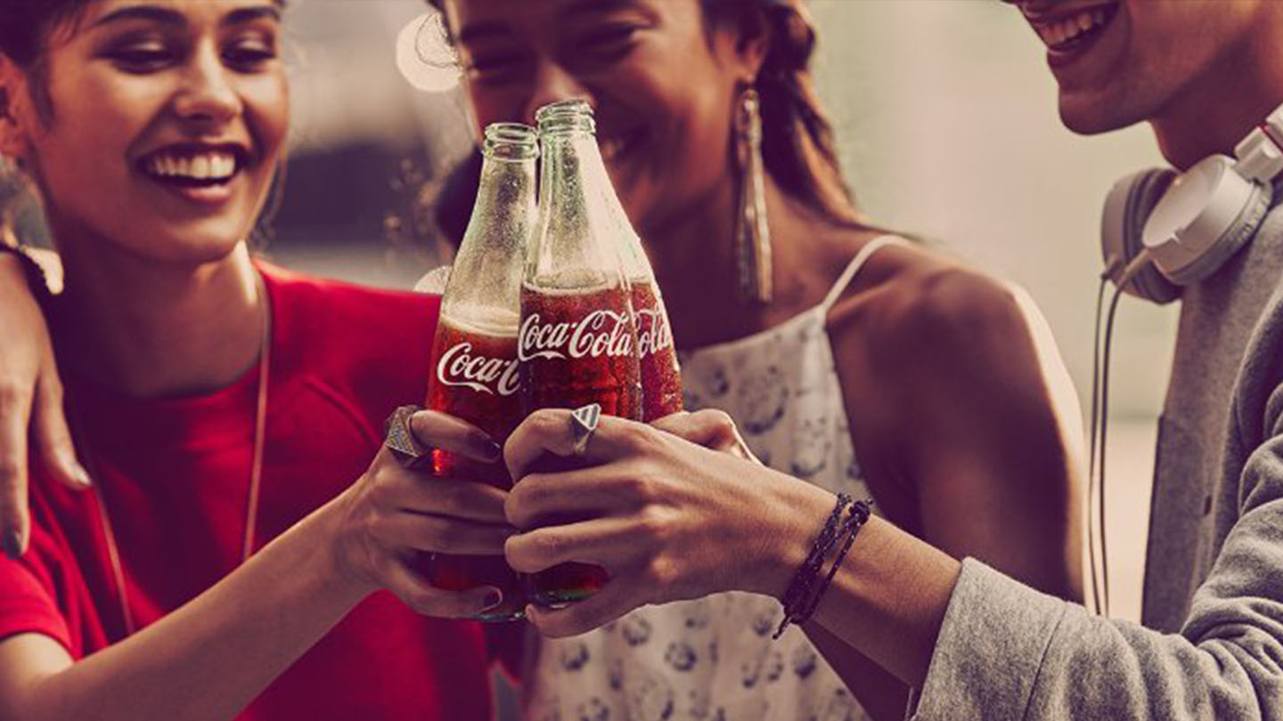 Group of friends smiling and toasting with three Coca-Cola bottles