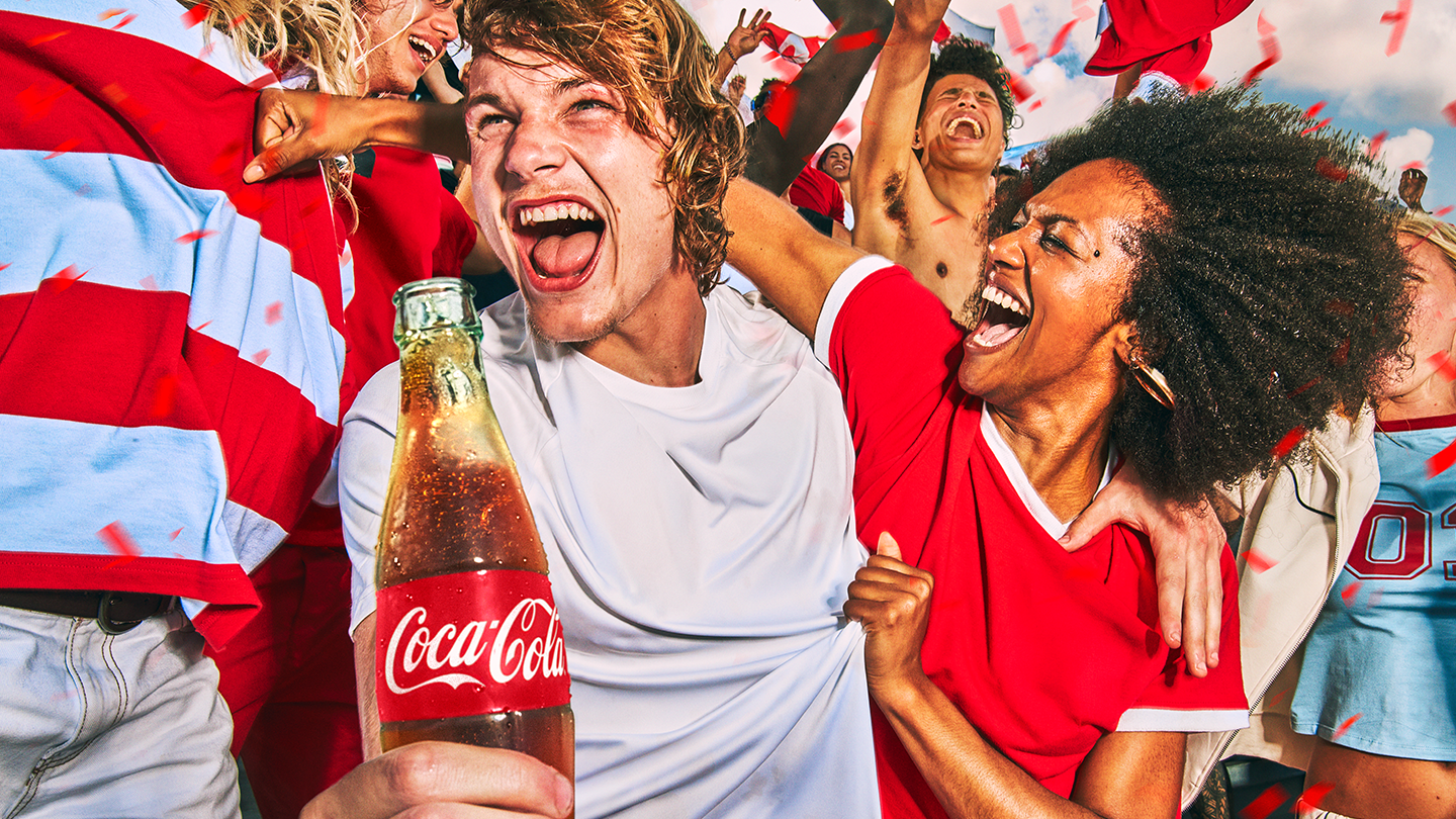 코카-콜라를 들고 월드컵 경기를 직관하며 열정적으로 응원하는 팬의 모습.