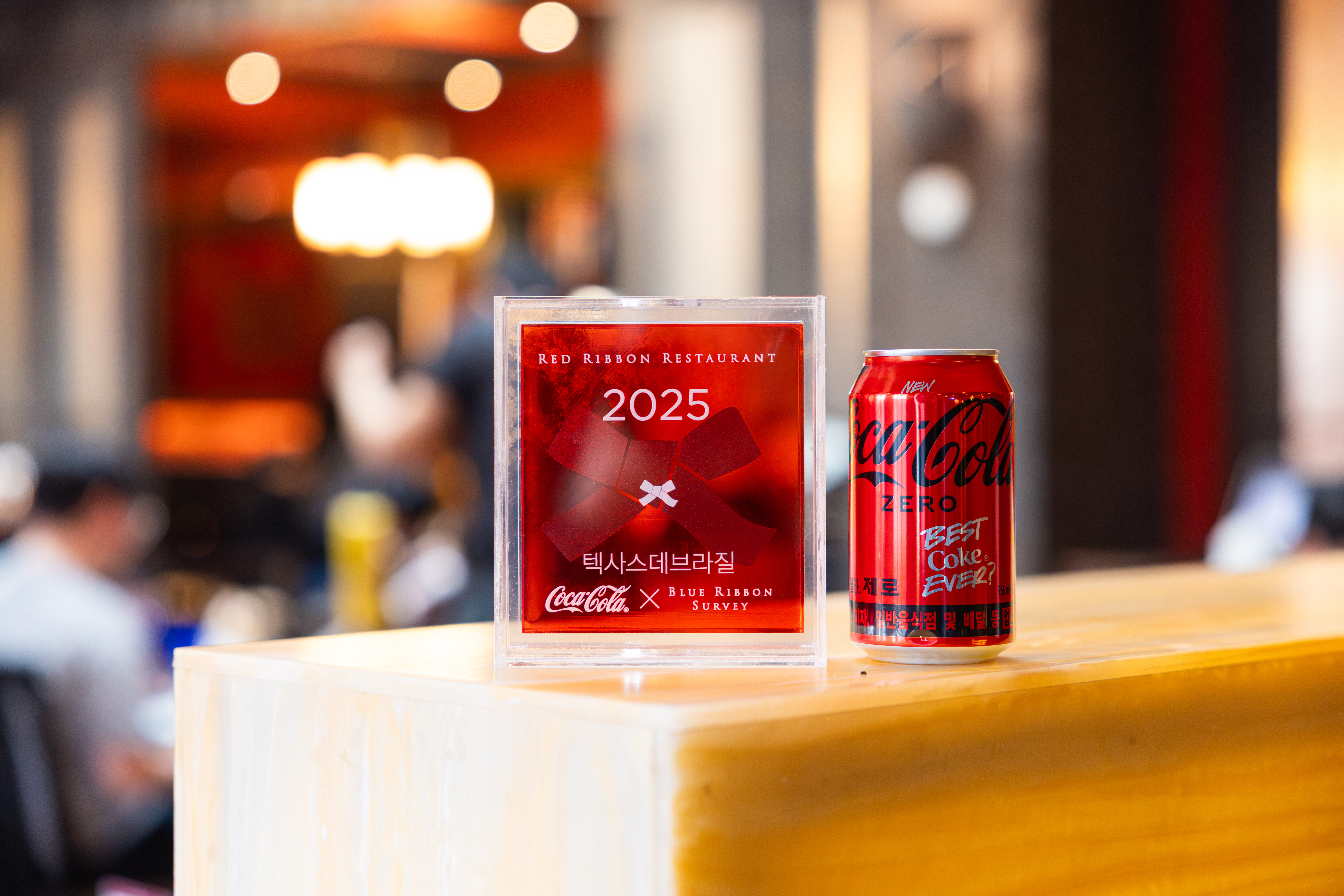 인증 받은 레드리본 맛집 '텍사스데브라질' 입구에 레드리본 명패와 코카-콜라 제로가 진열되어 있는 모습