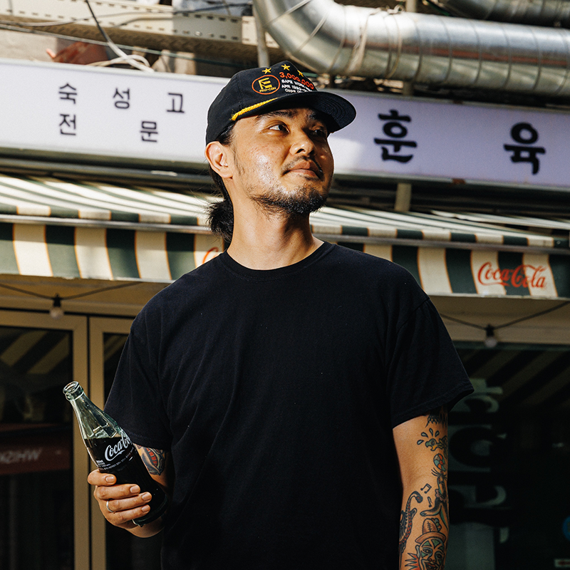 신흥시장 훈육 안훈 사장이 가게 앞에서 코카-콜라 병을 들고 서 있는 모습.