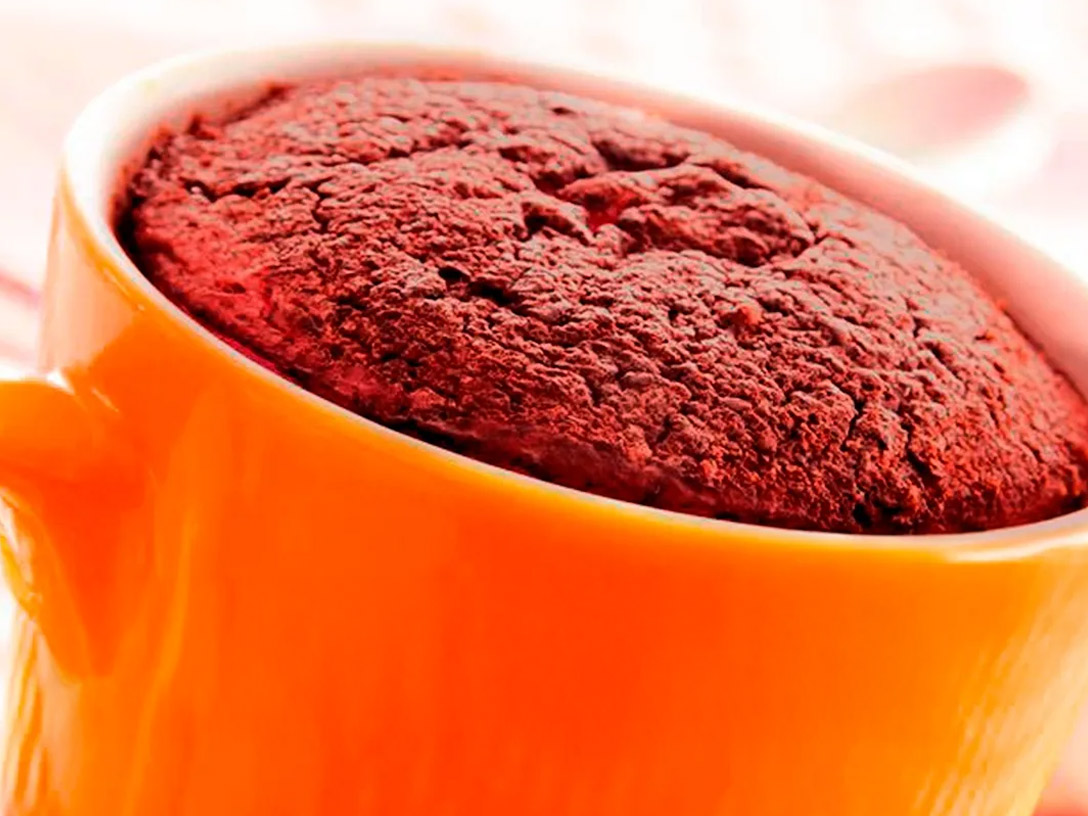 Una toma de cerca de un mug cake de chocolate en una taza naranja, con el texto "CHOCOFLAN MUG CAKE POR DANY ORBAN" en la parte inferior