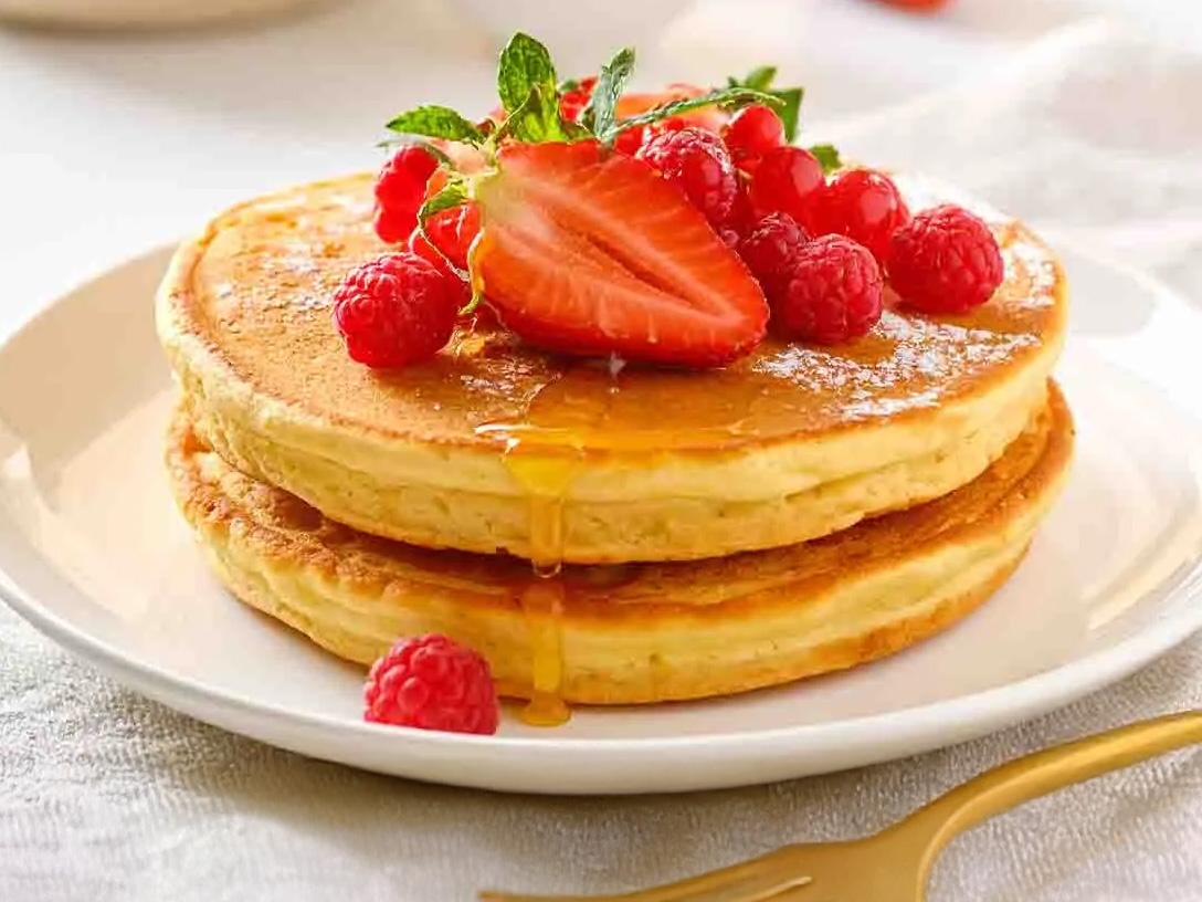  Una imagen de hot cakes con fresas y frambuesas encima, con el logo de Santa Clara y el texto "HOT CAKES PREPÁRALOS CON LECHE SANTA CLARA".