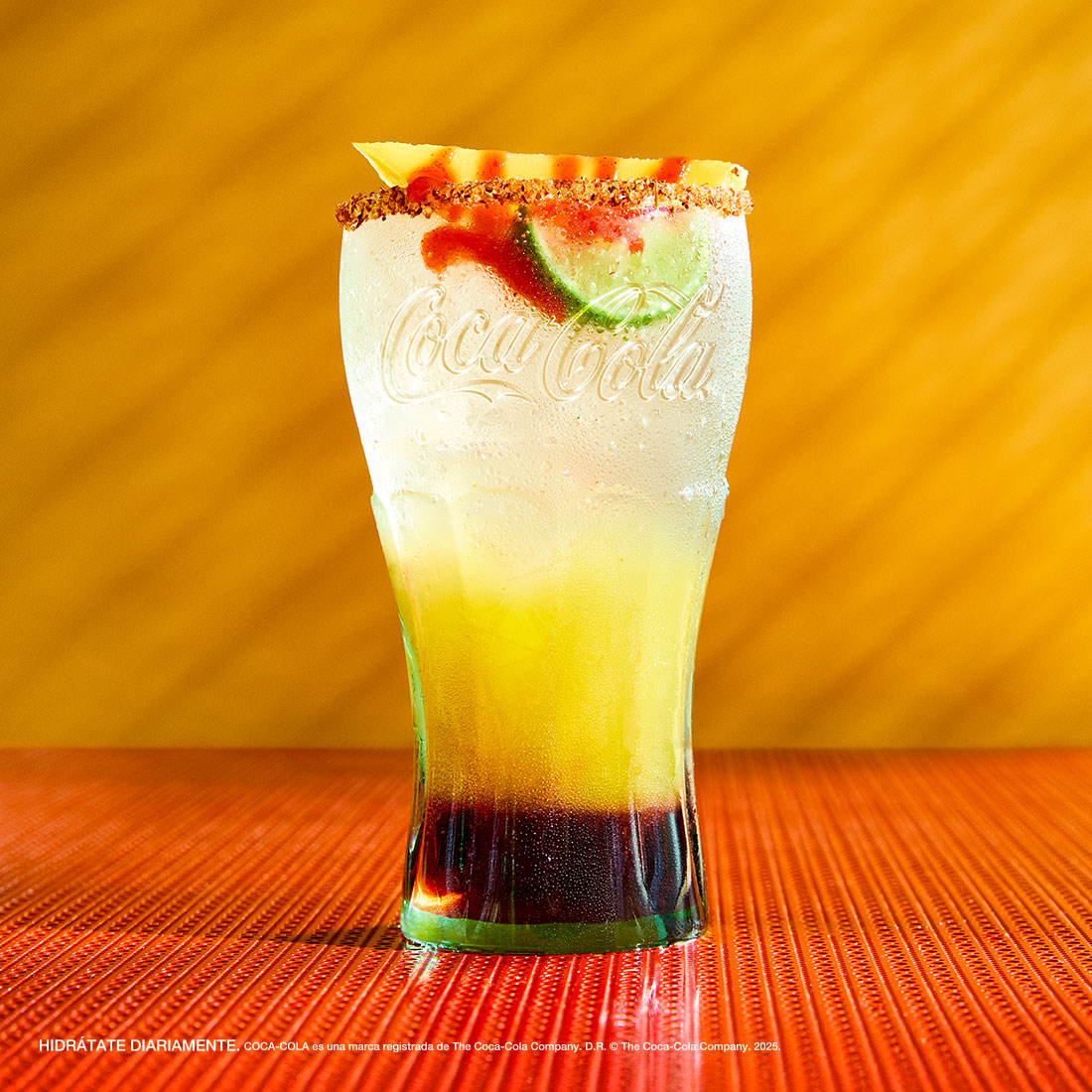 Bebida exclusiva de House of Coca-Cola servida en vaso de vidrio con limón y borde escarchado, sobre fondo amarillo.​