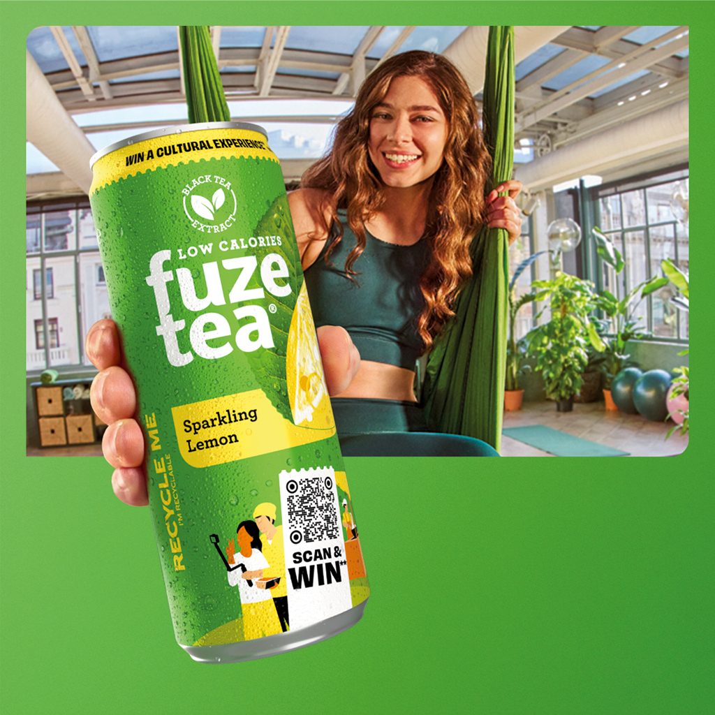 Personne tenant une canette de Fuze Tea dans une salle de sport lumineuse.