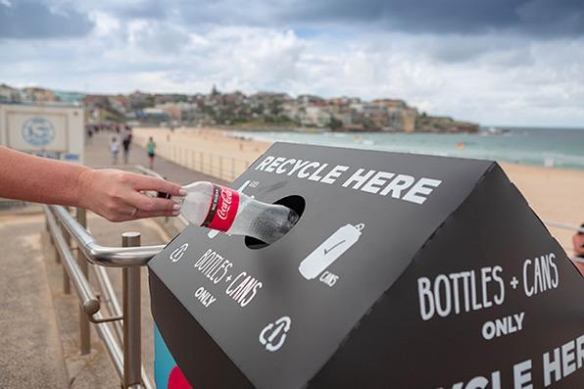 Detail of a hand putting an empty Coca-Cola plastic bottle in a recyclable trash bin