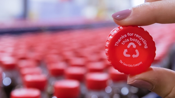 Detail of fingers holding a plastic bottle cap in front of various Coca-Cola bottles