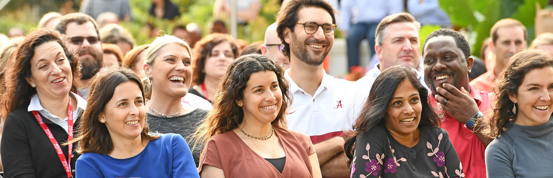 A large group of people laughing and smiling while watching something outdoors