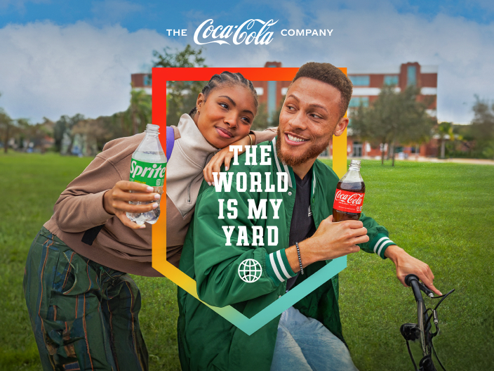 Girl and guy outside on green grass holding Coca-Cola products with the words "The Coca-Cola company, the world is my yard" overtop the image