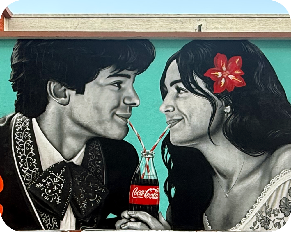 Los Otros Coca‑Cola mural showing a couple sharing a Coke with two straws for the Paint the Nation campaign.