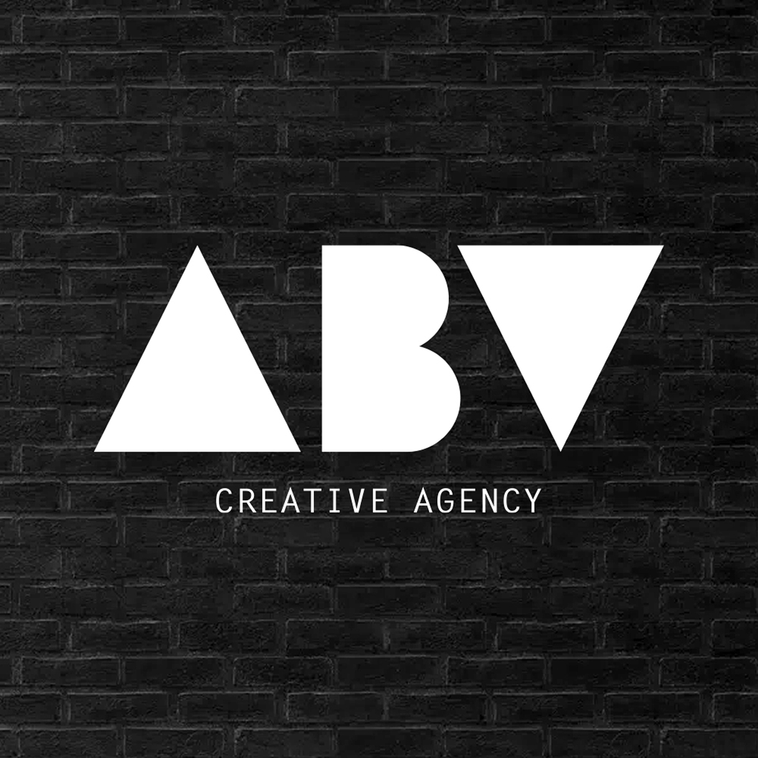 The white geometric logo for ABV Creative Agency, a partner on the Coca-Cola Paint the Nation project, on a black brick wall.