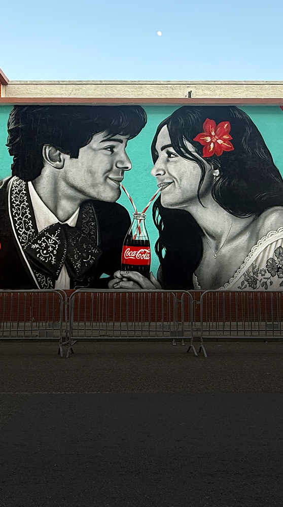 A beautiful mural in Brownsville, TX, of a couple sharing a classic Coca-Cola bottle with two straws under the moonlight.