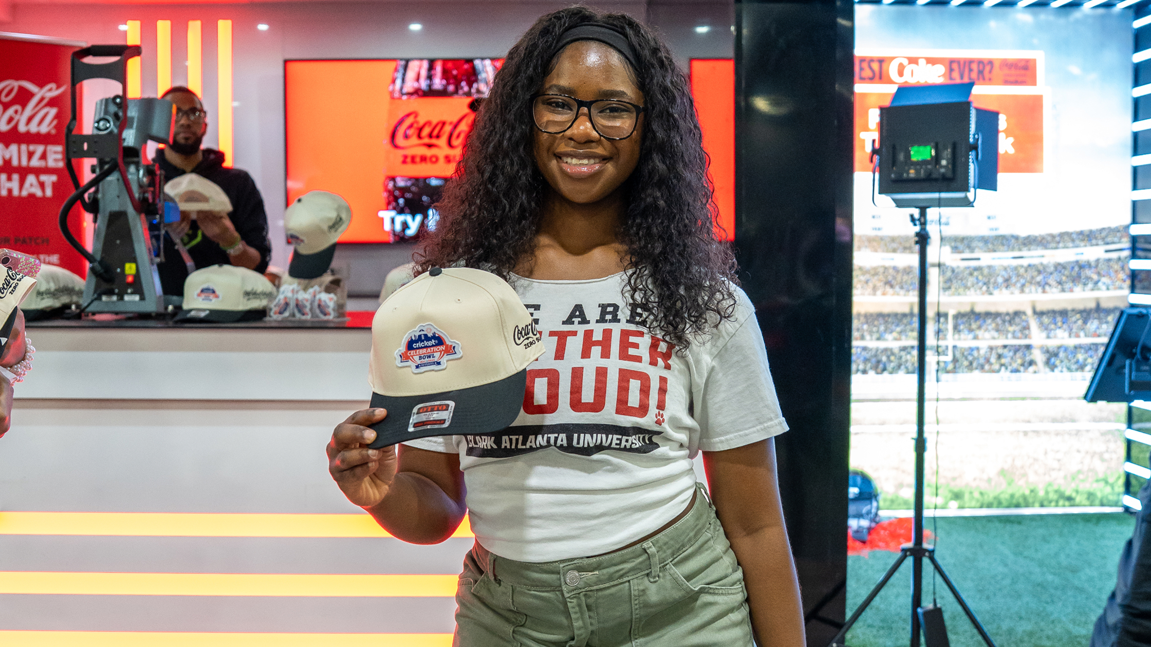 An HBCU student smiling and posing with a Celebration Bowl hat at a The World is My Yard activation