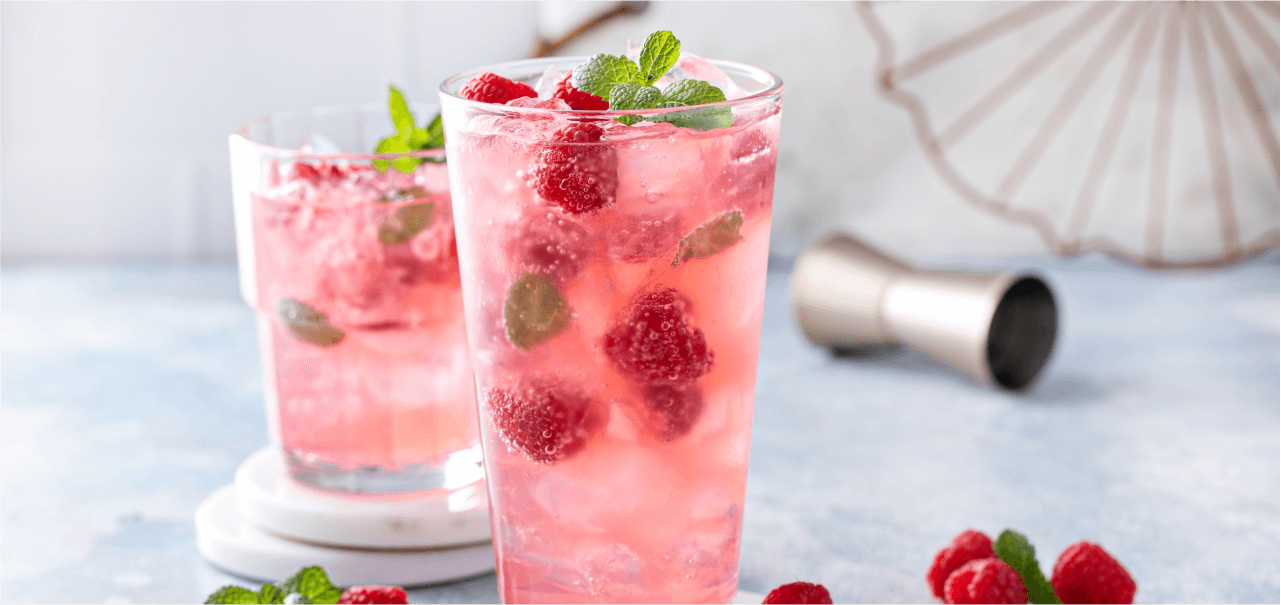 two tall pink drinks with garnish and raspberries