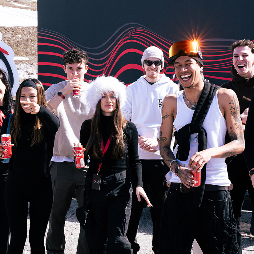 Un grupo de jóvenes sonrientes disfrutando de Coca-Cola en un ambiente de invierno, con ropa abrigada y lentes de sol.